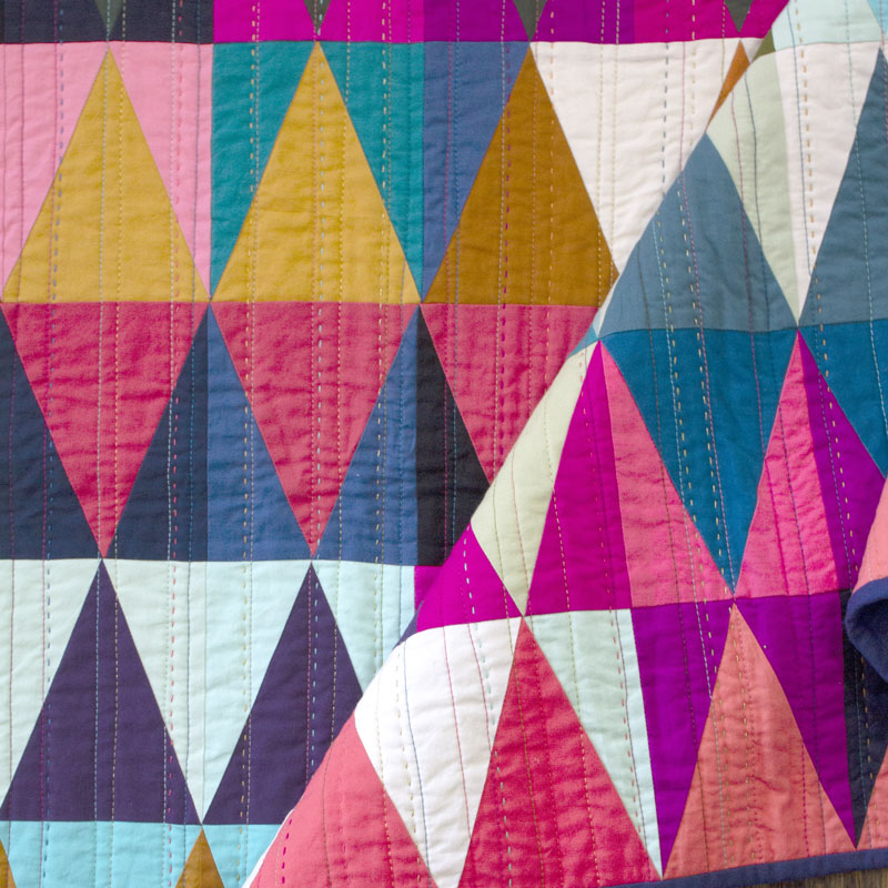 A folded close up of the colorful diamonds quilt showing hand and machine quilting.