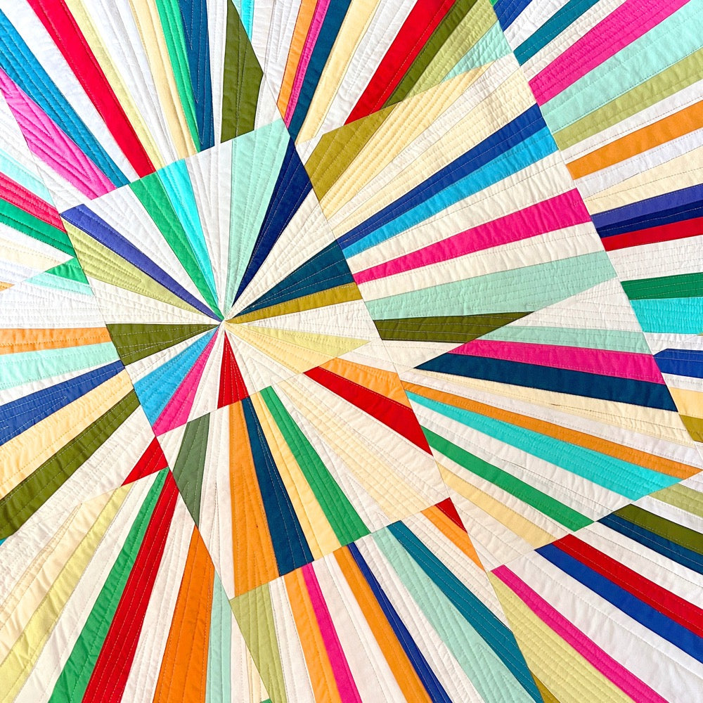 Close up of a colorful quilt with radiating lines and solid bright colored fabrics.