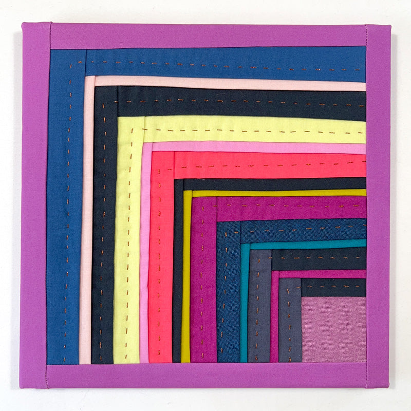 Small quilted wall art overlapping log cabin strips in jewel tone colors, with hand quilting in bronze thread.