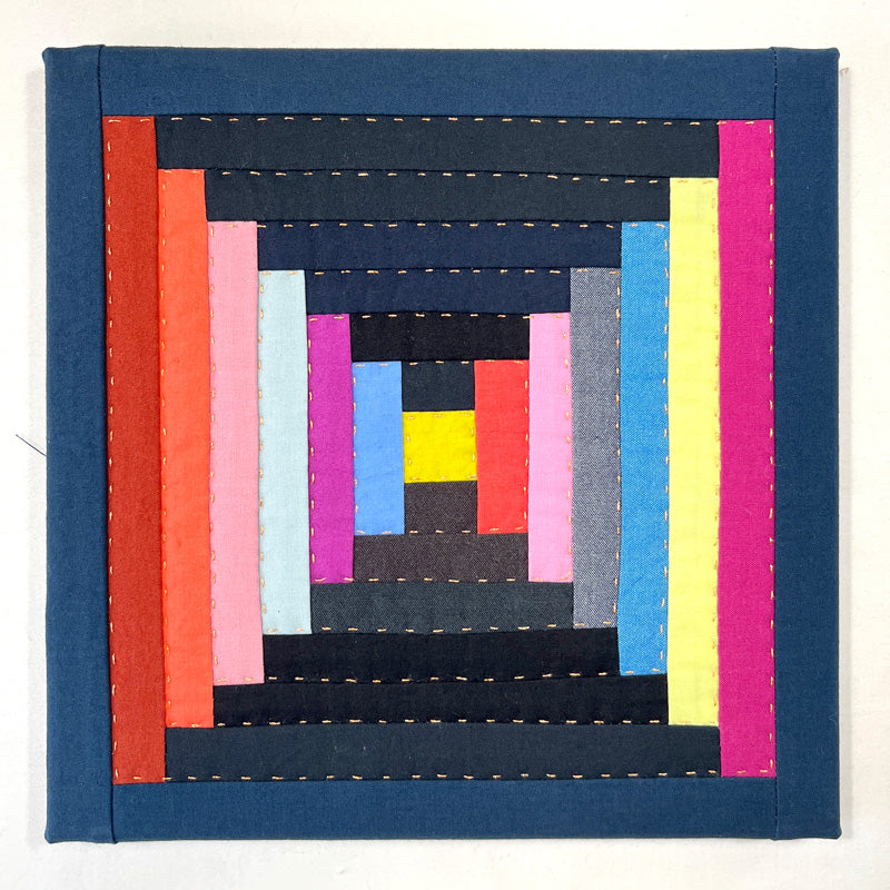 Small quilt wall art, in a log cabin pattern of jewel tones and dark blue. Hand quilted with metallic gold thread.