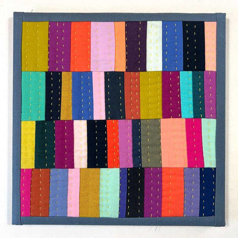 Small quilted wall art composed of rectangles, heavily hand quilted with bright yellow thread.