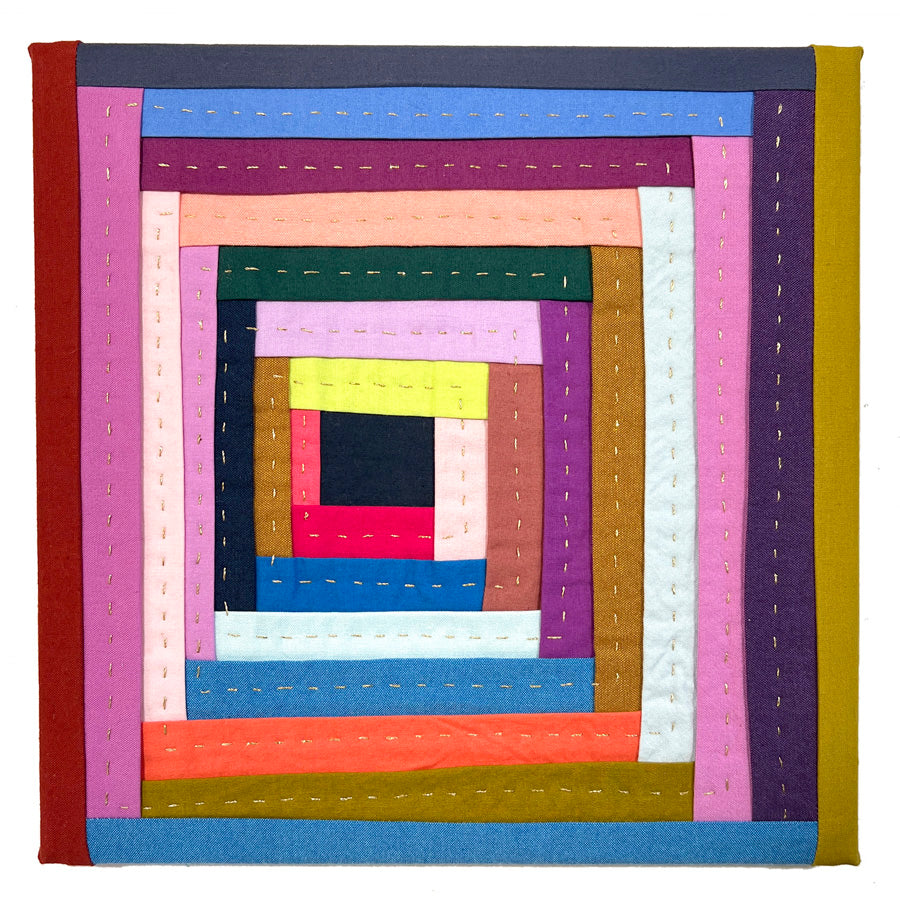 A small hand pieced log cabin quilted wall art made of folded fabrics in bright colors with metallic gold hand quilting.