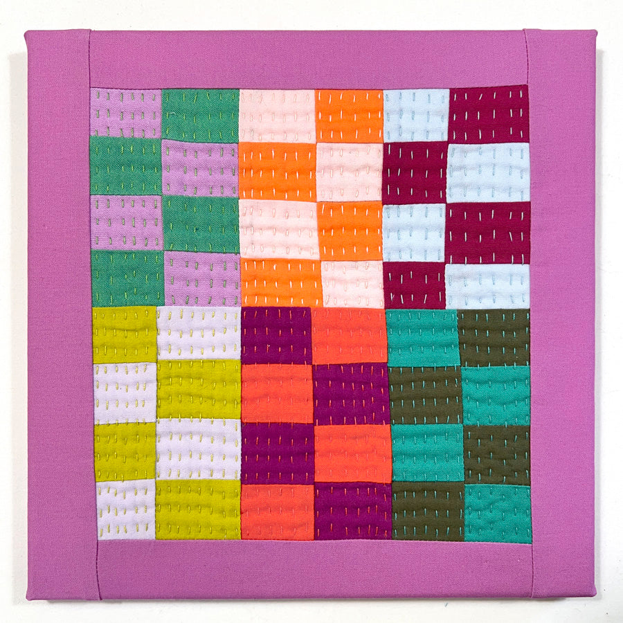 A small hand quilted wall art composed improvisational squares in multiple bright colors, stretched on canvas.