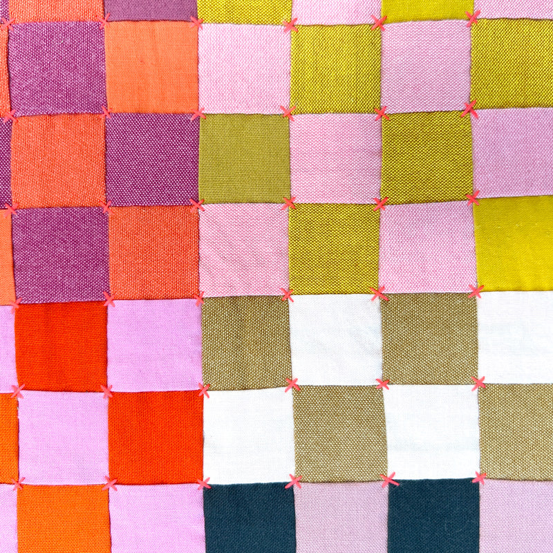 Close up of Small textile art made of square blocks in jewel tone colors with a small quilted accent.
