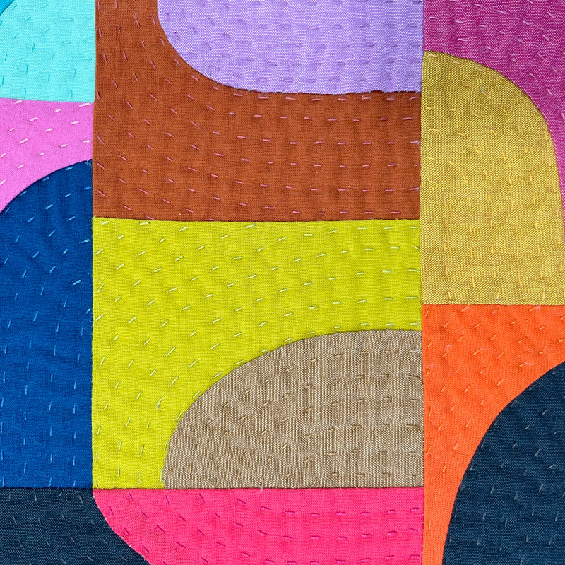 Close up of Small textile art made of curved drunkard's path blocks in jewel tone colors with hand quilting.