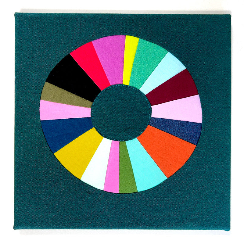 Small quilt art in bright jewel tone colors. The shape is a wonky circle on a green background.