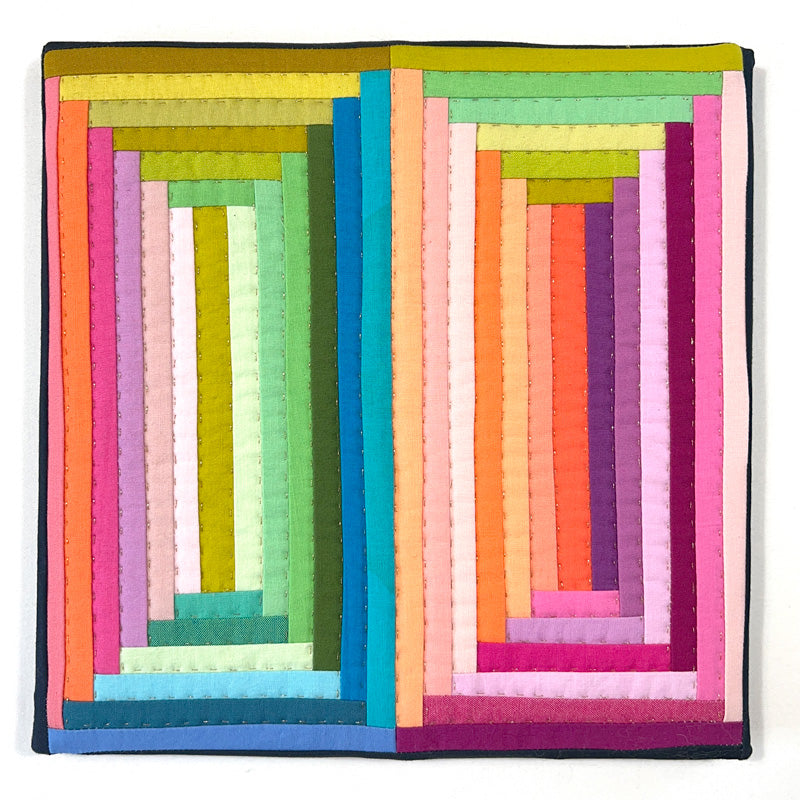 Small quilted wall art log cabin in bright rainbow colors with decorative gold hand quilting.