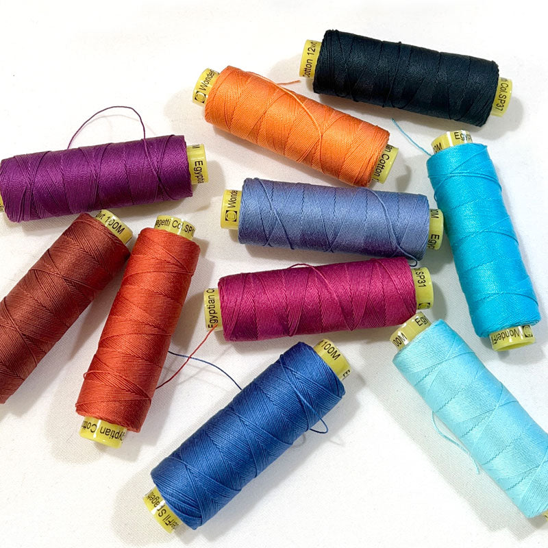 A collection of spools of hand quilting thread in a variety of colors arranged in a pile.
