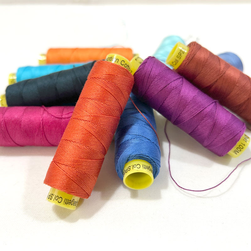 A collection of spools of hand quilting thread in a variety of colors arranged in a pile.