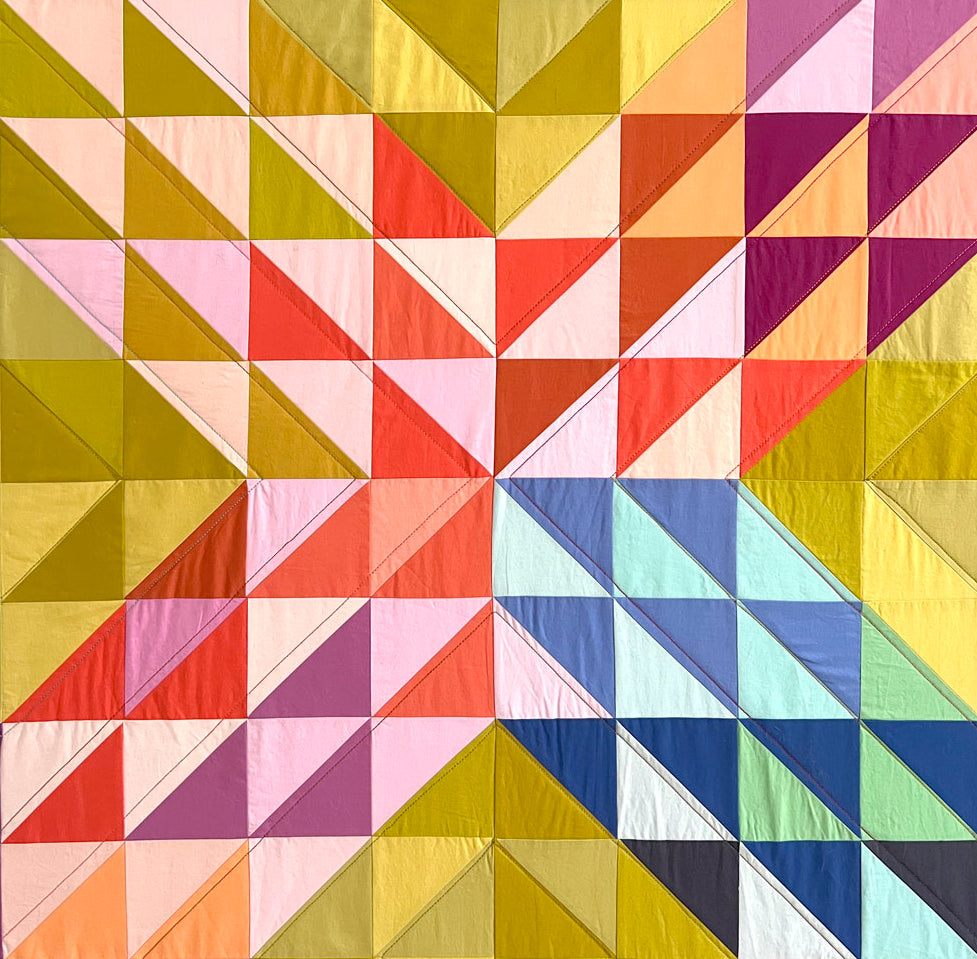 close up of colorful quilt made of half square triangle quilt blocks in an X shape with a yellow background