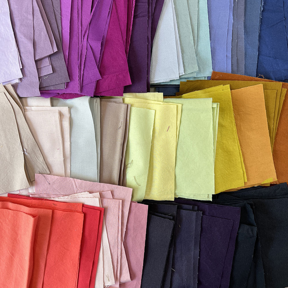A pile of rainbow colored fabrics cut into squares.