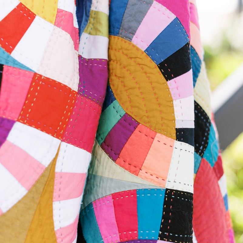 A close up of a folded Double Wedding Ring quilt in scrappy colors with hand quilting details.