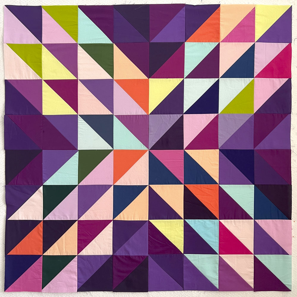 A baby quilt made of half square triangles in an "x" pattern. Made of rainbow colors and a purple background.