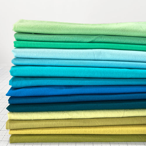 Stack of folded fabric sheets in green, blue, and yellow on a white background