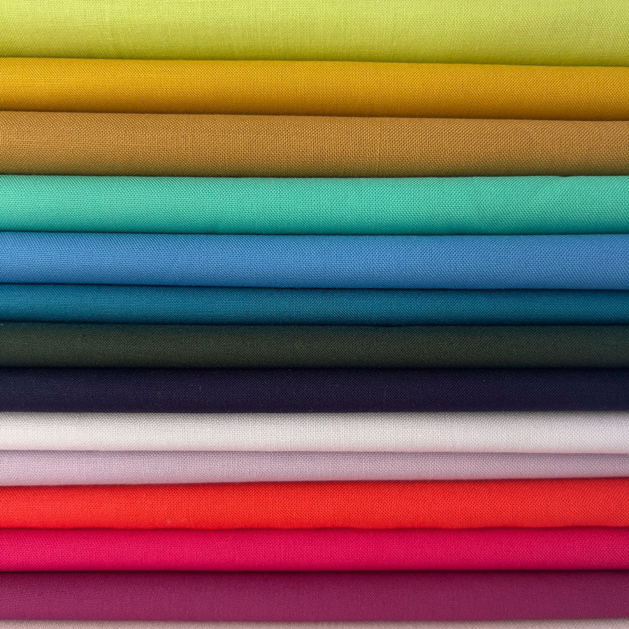 A stack of folded fabric swatches in a rainbow of colors, including yellow, orange, green, teal, blue, dark green, navy, white, pink, red, and purple, arranged horizontally.