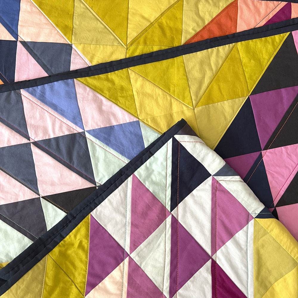 A close up pf a folded quilt made of half square triangles in an "x" pattern. Made of rainbow colors with a chartreuse background.