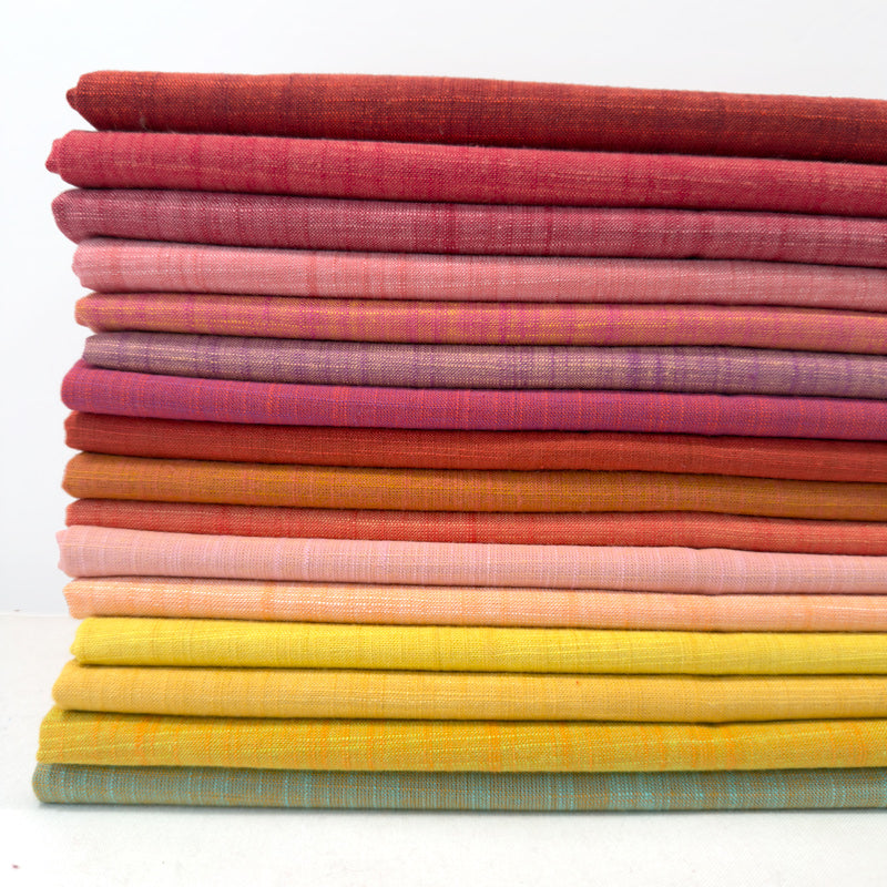 Stack of colorful fabric swatches in various shades of pink, orange, yellow, and red on a white background.