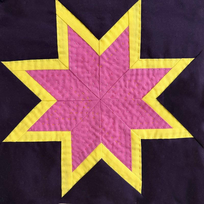 A close-up of a quilted star block featuring a bright pink center with yellow stitched borders and a dark purple background.