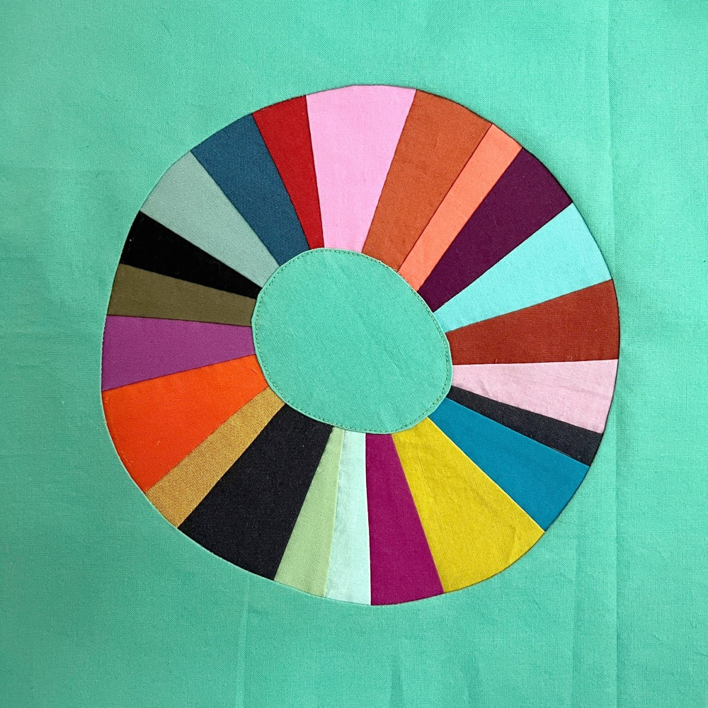 A wonky sewn circle on a green background. The circle is composed of wedges in multiple bright colors.