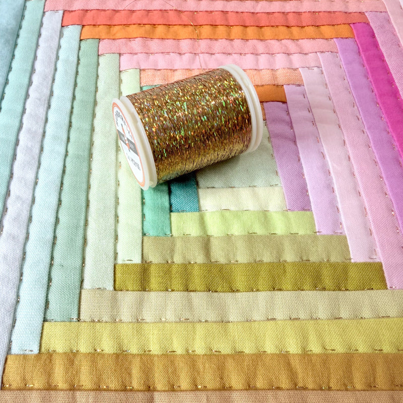 Spool of gold thread on a colorful quilt with pastel fabric strips