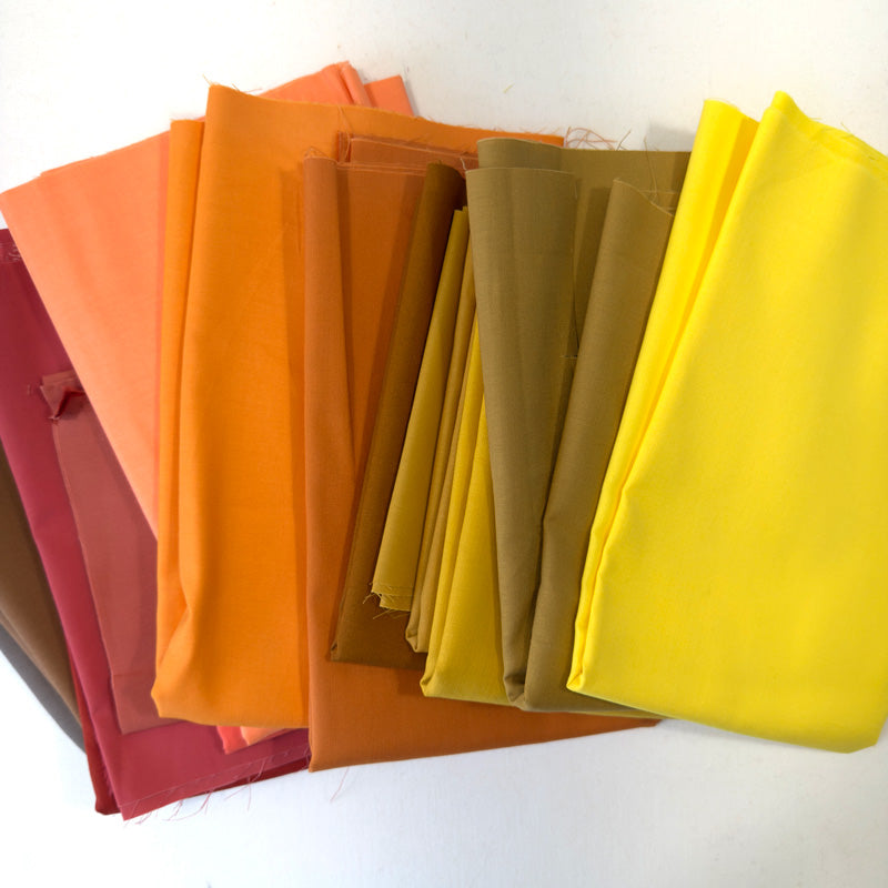 Stack of colorful fabric swatches in various shades including orange, yellow, and brown.