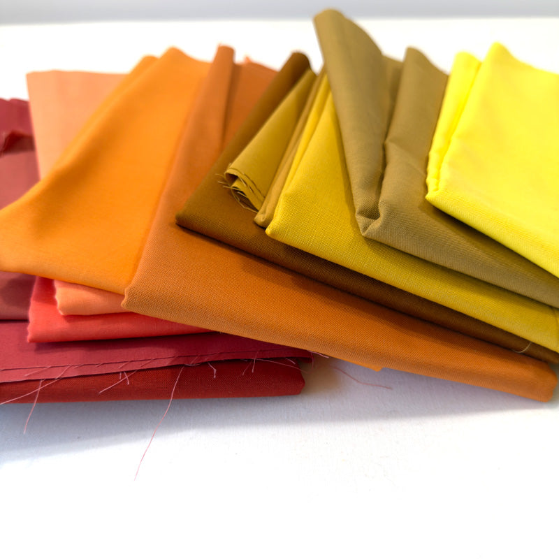 Stack of colorful fabric swatches in various shades including orange, yellow, and brown.