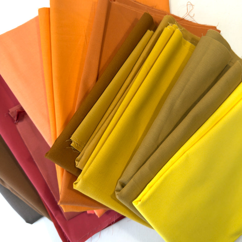 Stack of colorful fabric swatches in various shades including orange, yellow, and brown.
