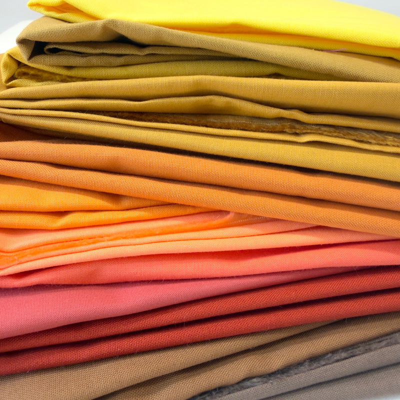 Stack of colorful fabric swatches in various shades including orange, yellow, and brown.