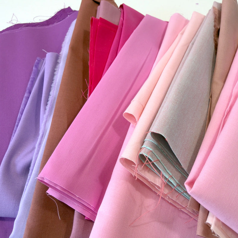 Collection of colorful fabric pieces in shades of pink and purple arranged in a row.