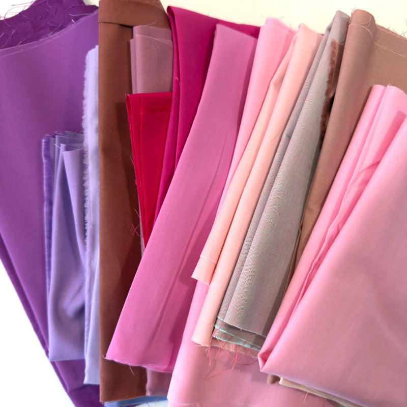 Collection of colorful fabric pieces in shades of pink and purple arranged in a row.