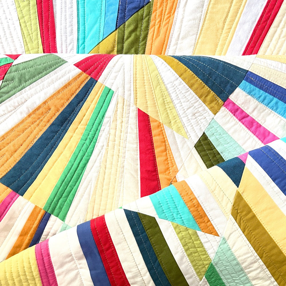 close up of a folded quilt with radiating lines and solid bright colored fabrics.