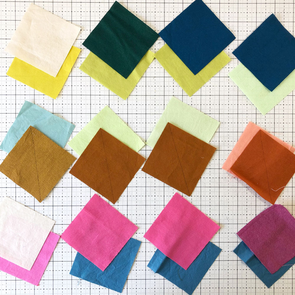 Half square triangle quilt blocks in progress on a cutting mat.