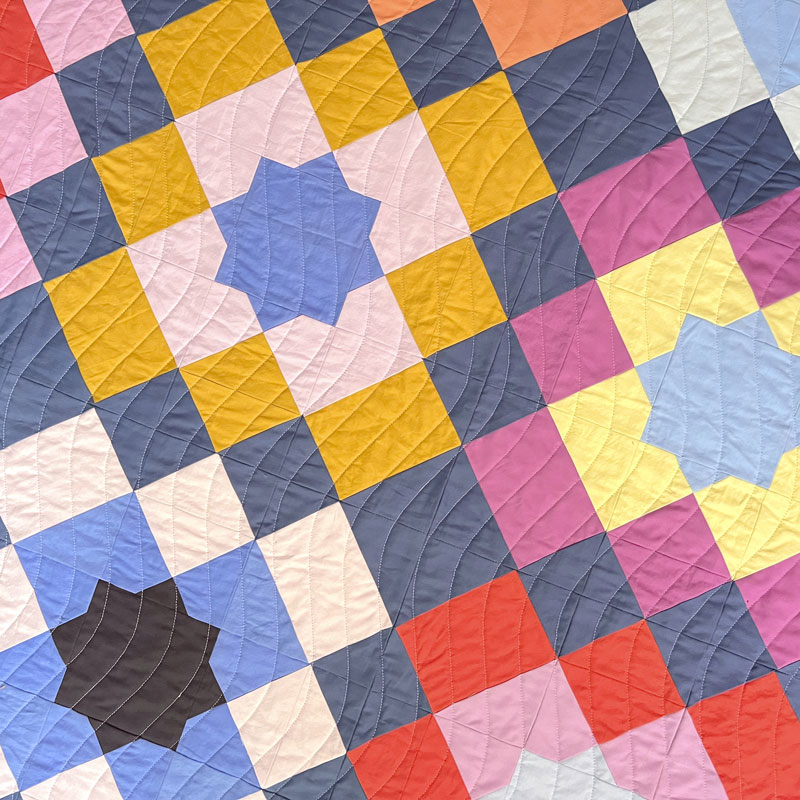 close up of marrakesh quilt showing wavy quilting lines. the quilt is multi colored with a dark blue background