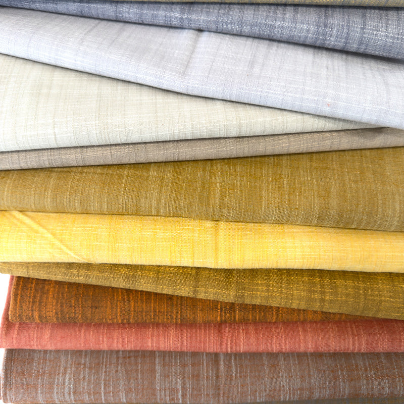 Stack of various textured fabrics in neutral colors.