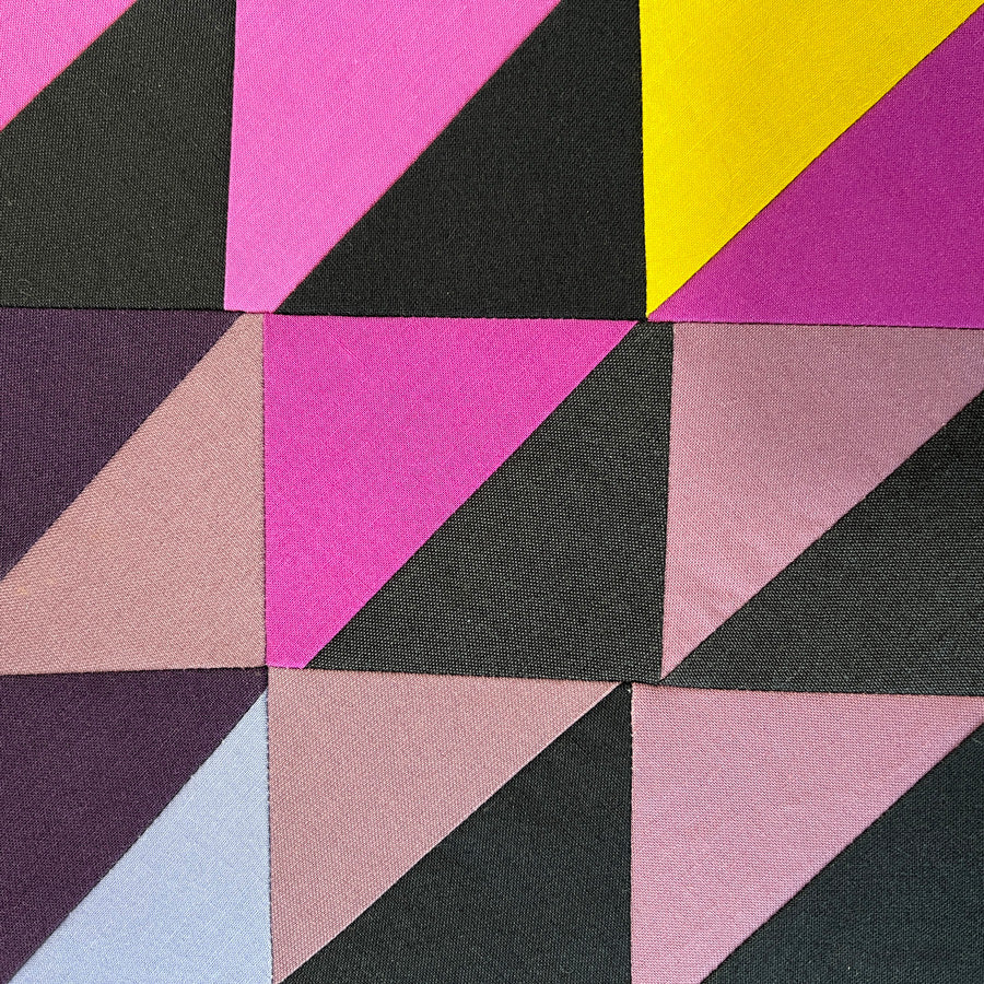 Close up of Small quilted wall art composed of half square triangle blocks in black, purple and yellow.