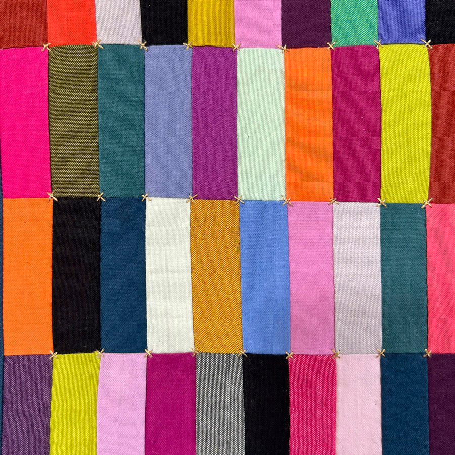 A close up of a small hand pieced quilted wall art quilted wall art made of multicolored rectangles and metallic gold hand embroidery.