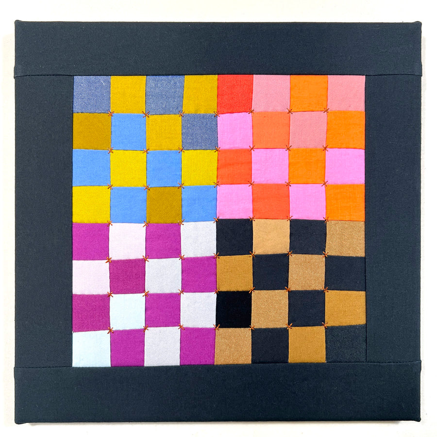 A small hand pieced quilted wall art quilted wall art made of multicolored square sin a checkerboard pattern with metallic gold hand embroidery.