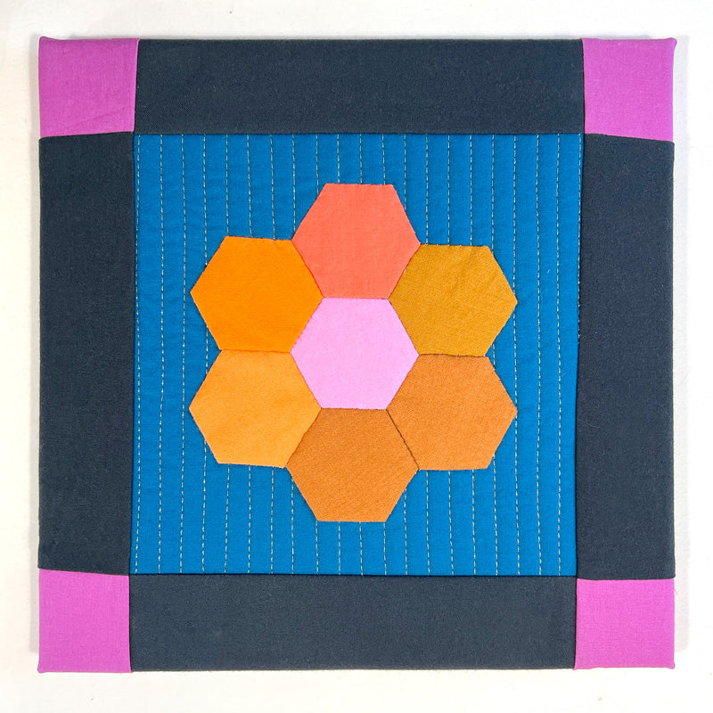 Small textile art made of hexagon blocks in jewel tone colors on a blue quilted background