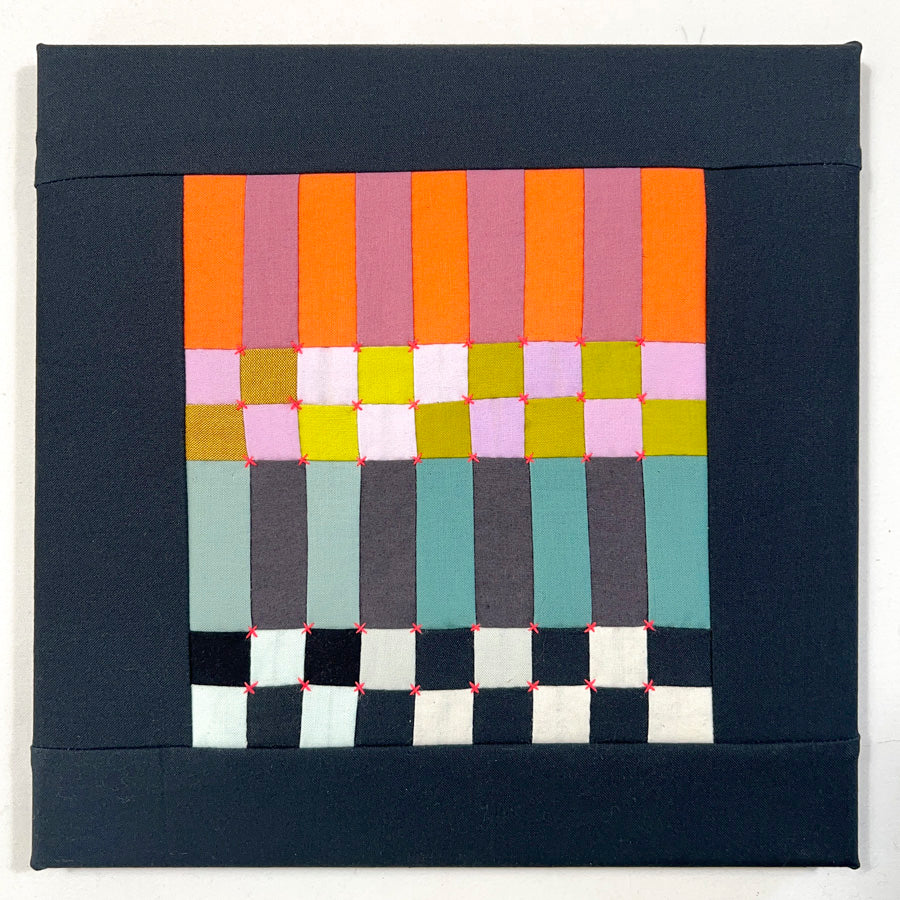 A small hand pieced quilted wall art made of squares and rectangles in multi colors with bright orange hand embroidery.