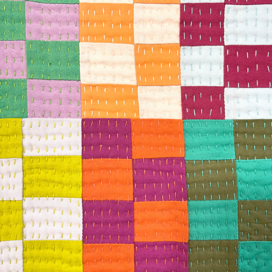 A close up of a small  hand quilted wall art composed improvisational squares in multiple bright colors, stretched on canvas.