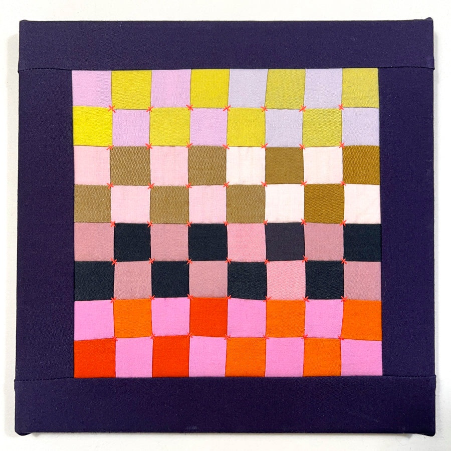 A small quilted wall art composed of multi colored squares  that is hand pieced, hand embroidered and stretched on archival acid free canvas.