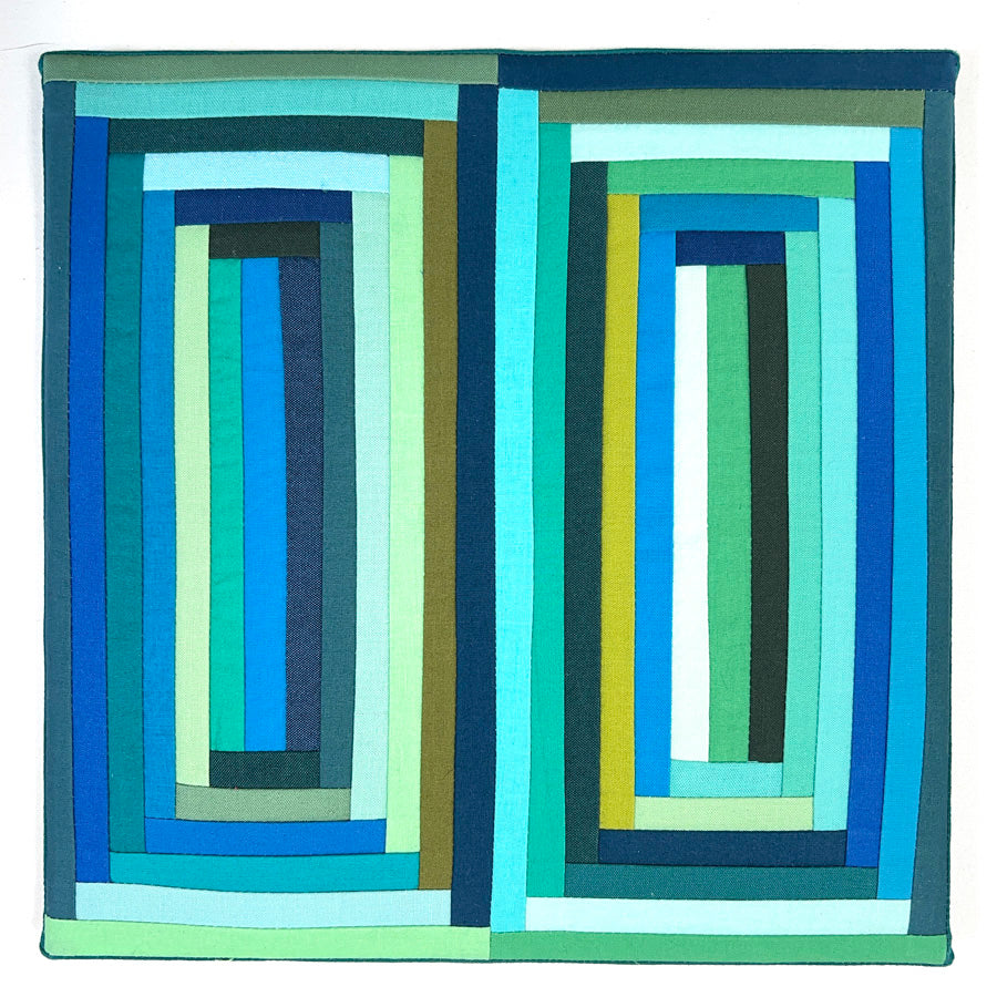 A small pieced rectangular  log cabin block made of green and blue colored  fabrics, stretched on a canvas.