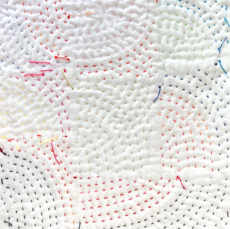 Close-up of white fabric with colorful thread stitches