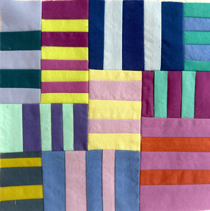 A close-up of a colorful patchwork quilt or fabric panel made of stitched rectangular blocks in various colors including pink, purple, blue, yellow, green, orange, and white.