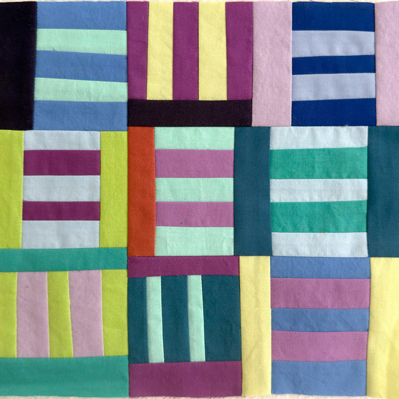 A square patchwork quilt featuring a colorful grid pattern of vertical and horizontal stripes in shades of blue, green, pink, yellow, purple, and orange.
