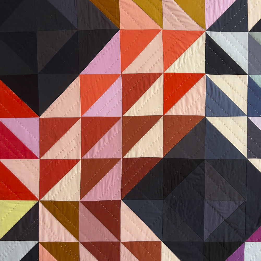 closeup of colorful quilt made of half square triangle quilt blocks in an X shape