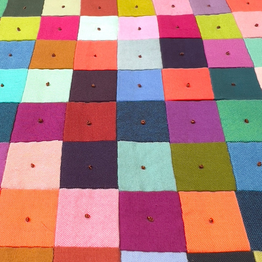 Close up of quilting detail on small quilt. Colorful squares and french knot embroidery.