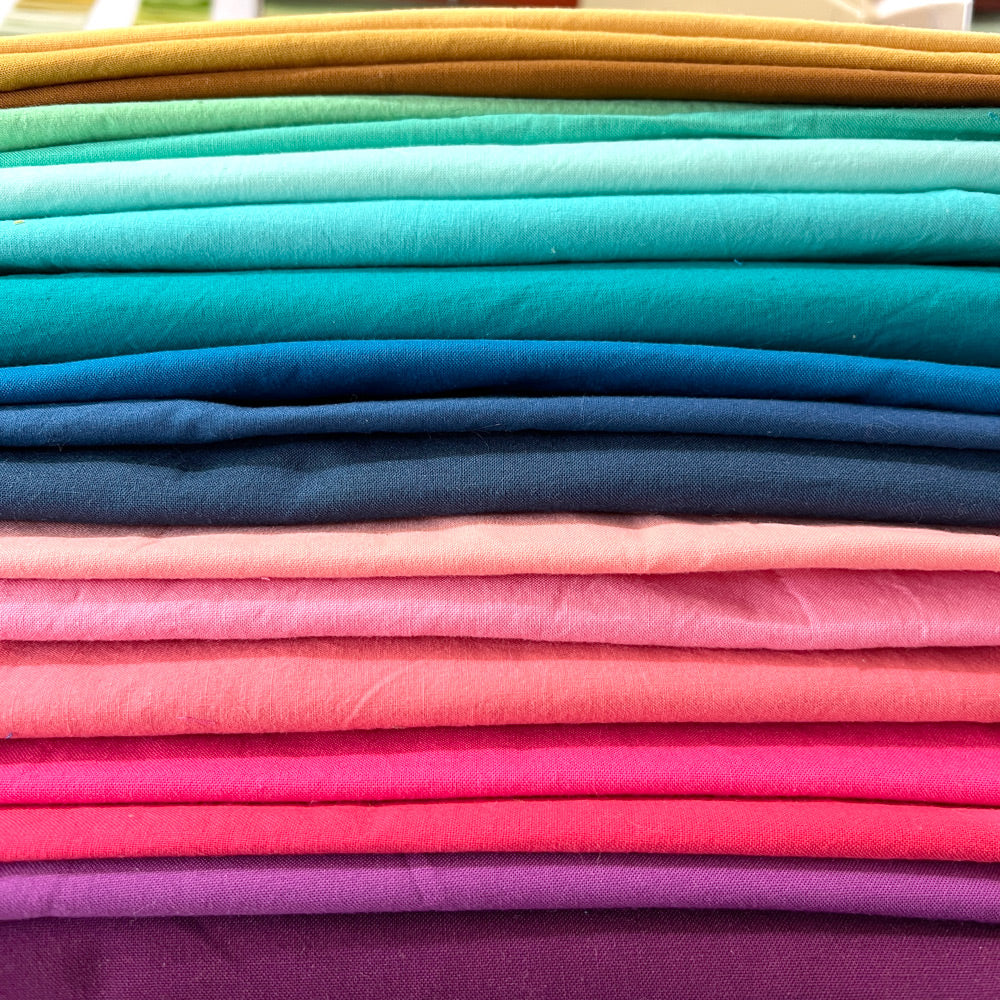 Pile of solid quilting fabrics in a rainbow of colors.