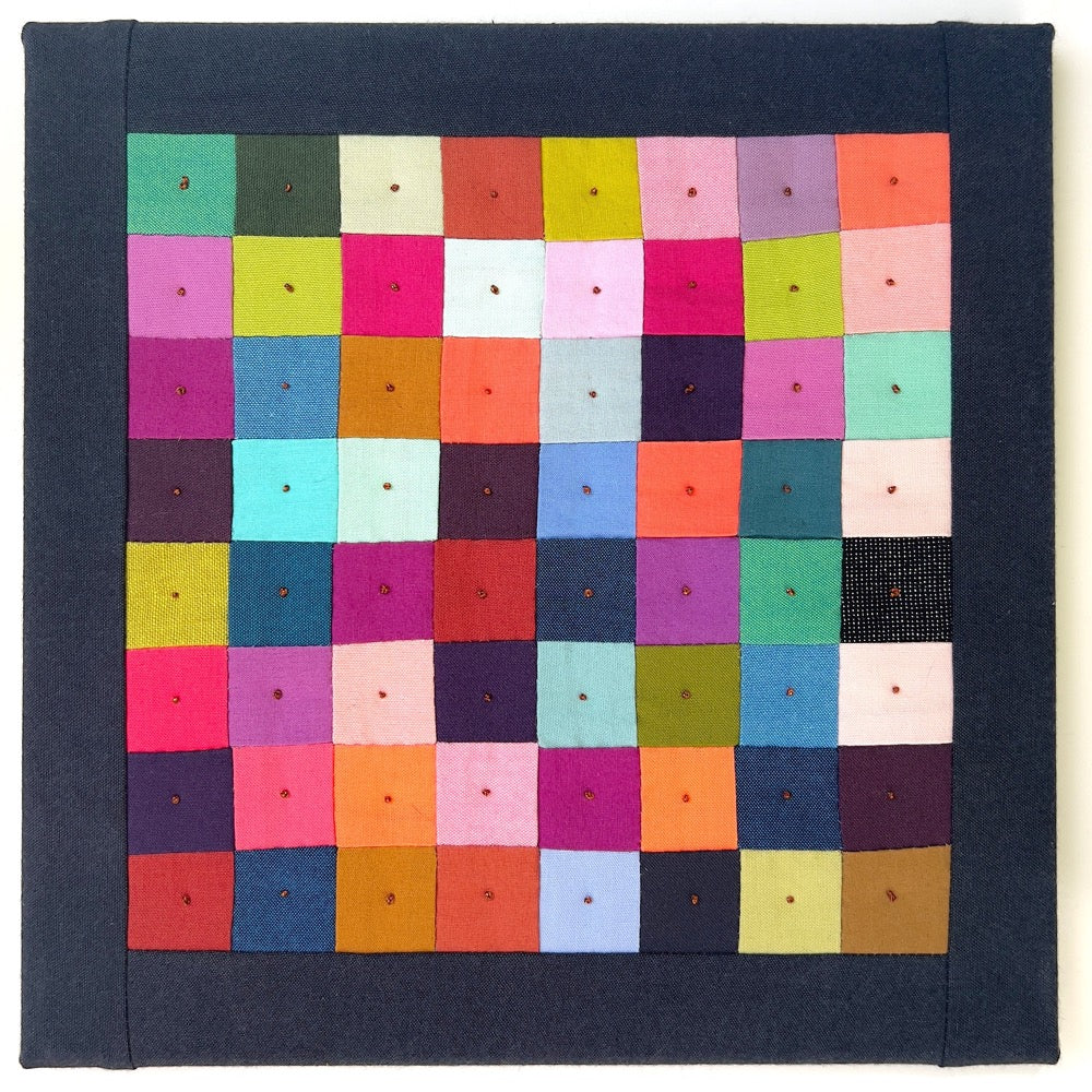 Small quilt made of multi colored squares with a black border.