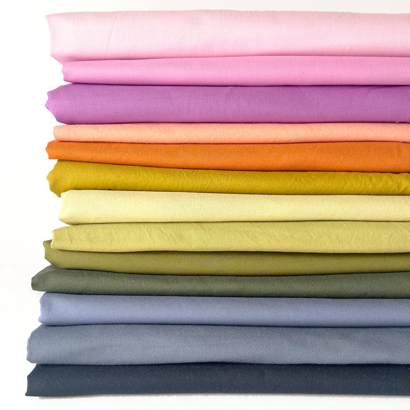 A stacked collection of folded fabric in a rainbow of colors, including pink, purple, orange, yellow, olive green, light blue, and navy, on a white background.